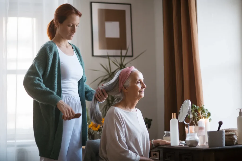 Carer assisting elderly woman with hair brushing and personal care at home in Sussex and Surrey